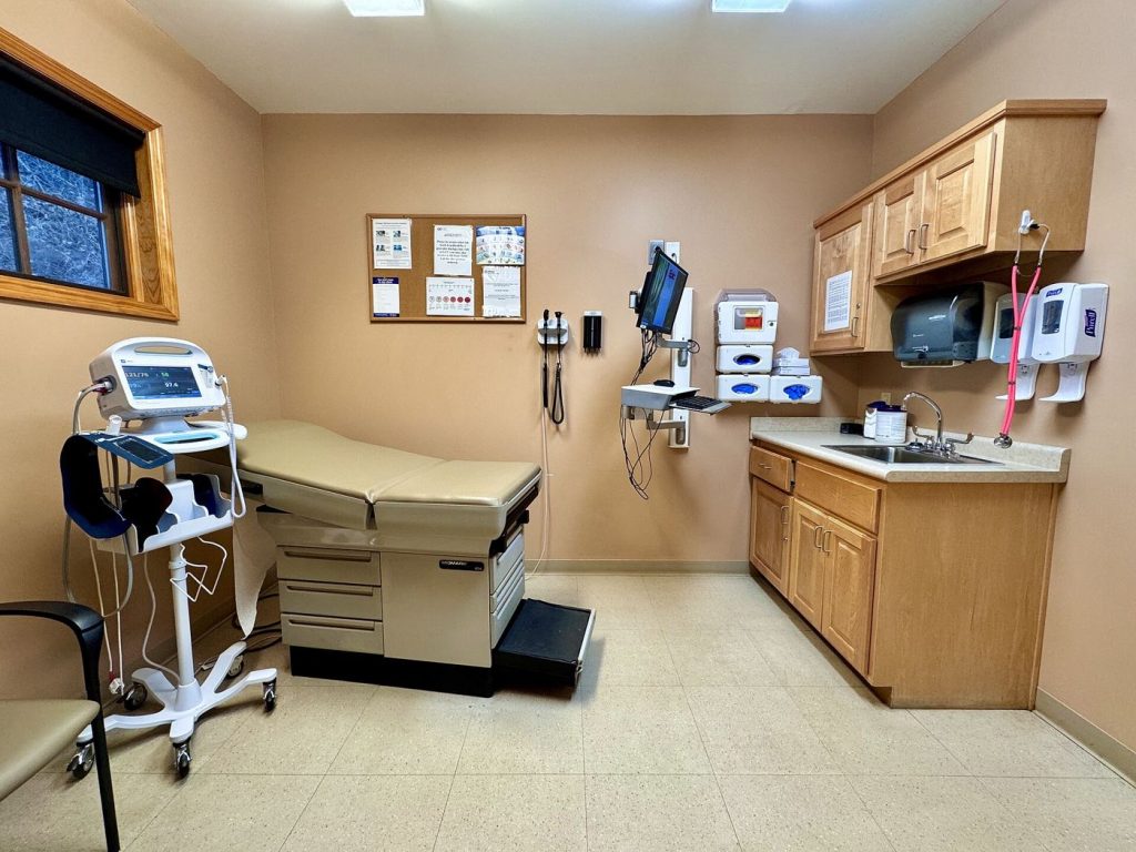 A doctor speaking with a patient during a clinic checkup in a bright examination room.